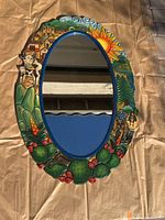 Full view of the oval mirror showing the entire carved and painted wooden frame with Southwest farm scene elements including cows, prickly pear cactus, buildings, trees, and sun.