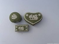 Three teal green Wedgwood boxes in typical jasperware style with white relief decoration, shown together to highlight shapes and detailing.