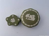Photo showing top view of two Jade green Wedgwood jasperware boxes, showcasing the white relief classical designs on lids.