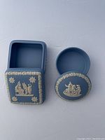 Two light blue Wedgwood jasperware boxes, one square and one round, side by side on a white surface, lids removed showing interiors