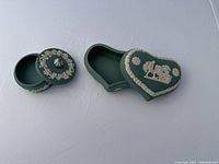 Two teal green Wedgwood jasperware boxes, one round and one heart-shaped, both with white relief decorations.