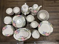 Top-down view capturing the full set laid out on a wood floor, showing plates, teapots, bowls, and platters with floral pattern.
