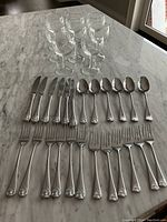 Cutlery arranged in rows showing 6 dinner knives, 6 dinner forks, 6 tablespoons, 6 salad/dessert forks, and 6 dinner cutters with decorative handles on a marble surface.