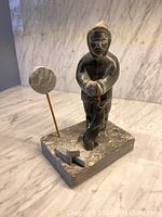 Front view of carving showing Inuit hunter holding seal on rectangular base with circular element on rod.