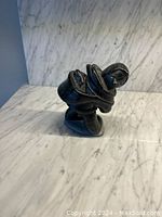 Full side view of the dark stone Inuit sculpture figurine on marble surface, showing the shape and posture.