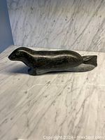 Side view of the dark stone seal sculpture showing smooth polish, facial detail, and tail.