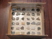 Box opened showing 40 rock chip samples mounted on gridded cardboard backing, displaying variety of mineral types, colors and textures.