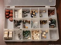 Top-down view of open compartment organizer showing small wooden beads, metal findings, and various small beads separated by compartments.