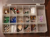 Top-down image of the clear plastic organizer box with multiple compartments filled with various beads and pendants in different colors and shapes, showing organization and contents clearly.
