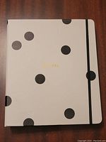 Front cover of Kate Spade recipe binder featuring black polka dots, gold 'Recipes' lettering, and black elastic closure.