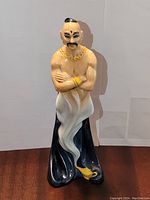 Front view of Royal Doulton The Genie HN 2989 figurine showing crossed arms, gold jewelry, white swirling base, and dark blue cape.