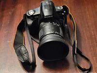 Front view of Sony Alpha A230 DSLR camera with attached Sigma lens and strap on wooden surface.