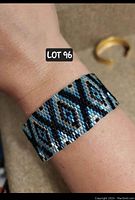 Bracelet worn on wrist to show fit and pattern of geometric diamond shapes in blue, silver and black beads with shimmer.