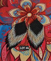 Close-up photo of a pair of hand-beaded tassel earrings with a black and white bead pattern and silver accents, laid on a colorful floral fabric background.