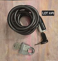 Coiled cable bike lock with black grip and metal padlock alongside two keys for each lock, laid on wooden surface.