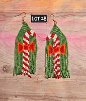 Pair of green, red, white, and orange hand-beaded tassel earrings with candy cane motif, displayed flat on wooden surface.