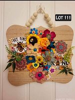 Front view of the wooden floral sign showing the 'Bee Kind' text, colorful flowers, and bee decals.