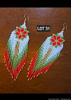 Pair of hand-beaded Christmas poinsettia tassel earrings laid flat on a wooden surface showing detailed beadwork and color pattern.