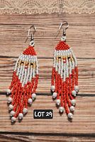 Pair of hand-beaded Santa tassel earrings in red, white, and flesh-tone beads with tassel fringe and nickel-free hooks on a wooden background with lace top border