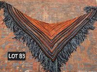 Full view of triangular hand-knit shawl laid flat showing the overall pattern, colors in orange, brown, and blue with fringe edges.