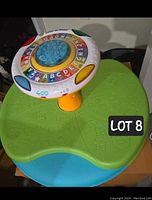 Front view of LeapFrog Letter-Go-Round toy on green and blue base showing alphabet letters, speaker grills, and colorful design.