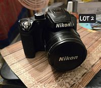 Nikon Coolpix P500 camera front angled view showing lens with Nikon lens cap and body with some wear