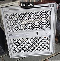 White plastic extendable pressure mounted baby/pet gate with lattice pattern and latch mechanism, shown folded/laid flat.