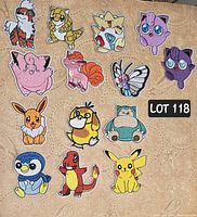 Photo of 14 Pokémon embroidered patches on light patterned fabric background, arranged in a grid pattern, showing full colors and details of each patch.