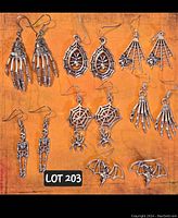 Photo showing seven pairs of silver-toned Halloween-themed dangle earrings arranged on an orange surface with lot number sticker visible