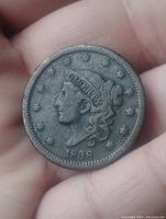 Obverse side of the 1838 US Large One Cent coin showing Liberty head profile, date, and stars with dark patina on a hand background.