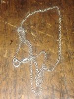 Silver Figaro chain necklace laid out on a wooden surface showing chain links and clasp.