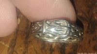 Close up of silver ring shaped as belt buckle showing woven design and tarnish needing cleaning.