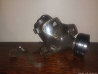 Side view of black rubber military gas mask with filter showing clear eye lenses and adjustable straps.