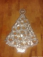 Front view of the pewter Christmas tree shaped item photographed on wood floor showing all holiday detail and star topper.