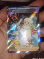 Photo showing Melony Trainer full art foil Pokémon card with holographic artwork, held by hand in good light to showcase condition and foil effects.