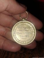 Back side of the medal held in hand with close-up to display the inscription and detail.