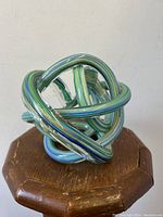 Full view of the endless knot art glass sculpture highlighting the green and blue striped pattern on a wooden base.
