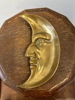 Top view of the crescent shaped metal tip tray showing the detailed figural man in the moon face against a wood surface.