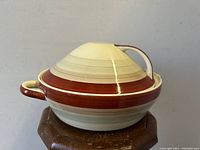 Front angle of lidded casserole dish showing banded stripes and conical lid with handle.