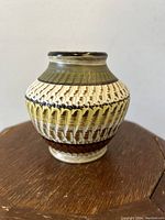 Overall front view of rounded small Dumler & Breiden pottery vase with textured vertical and horizontal pattern in earth tones on wood surface.