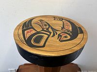 Top view of the closed circular cedar bentwood box showing painted Haida design with animal motifs and artist signature.