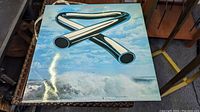 Front cover of Mike Oldfield Tubular Bells vinyl LP showing iconic tubular bells graphic on cloudy blue sky background.