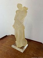 Side view of yellow-tinted translucent Pierrot Harlequin clown figure holding stringed instrument, mounted on clear rectangular Lucite base.