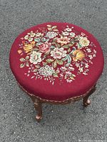 Top angle view showing needlepoint floral bouquet tapestry on burgundy fabric upholstery and carved wood frame with upholstery tacking