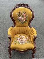 Front view of armchair showing carved crest and needlepoint upholstery