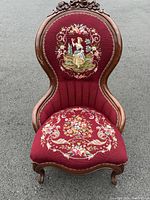Front view of chair showing carved crest, high back pastoral needlepoint scene and floral seat motif