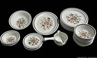 Full view of the set arranged showing plates, bowls, and small handled dish with floral pattern and brown rim bands.