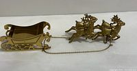 Photo showing brass sleigh and four attached reindeer, polished surface and chain connection visible.