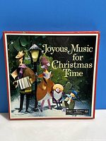 Front view of the box showing the title and artwork with carolers and a lantern under a tree.