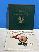 Front covers of two vintage Christmas record albums featuring Bing Crosby. One is green with gold text and bells illustration, titled 'King Out Christmas Bells'. The other is red with gold text, titled 'Twelve Famous Hymns' with bonus Merry Christmas sleeve showing Bing Crosby in Santa hat.